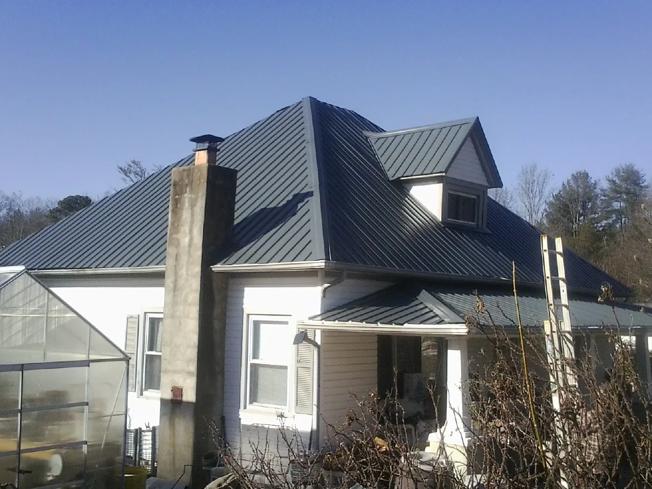 Dark blue standing seam metal roof on a white farmhouse with dormer — Slate & Tile Roof Repair by Roofing Brothers in Chestnut Mound