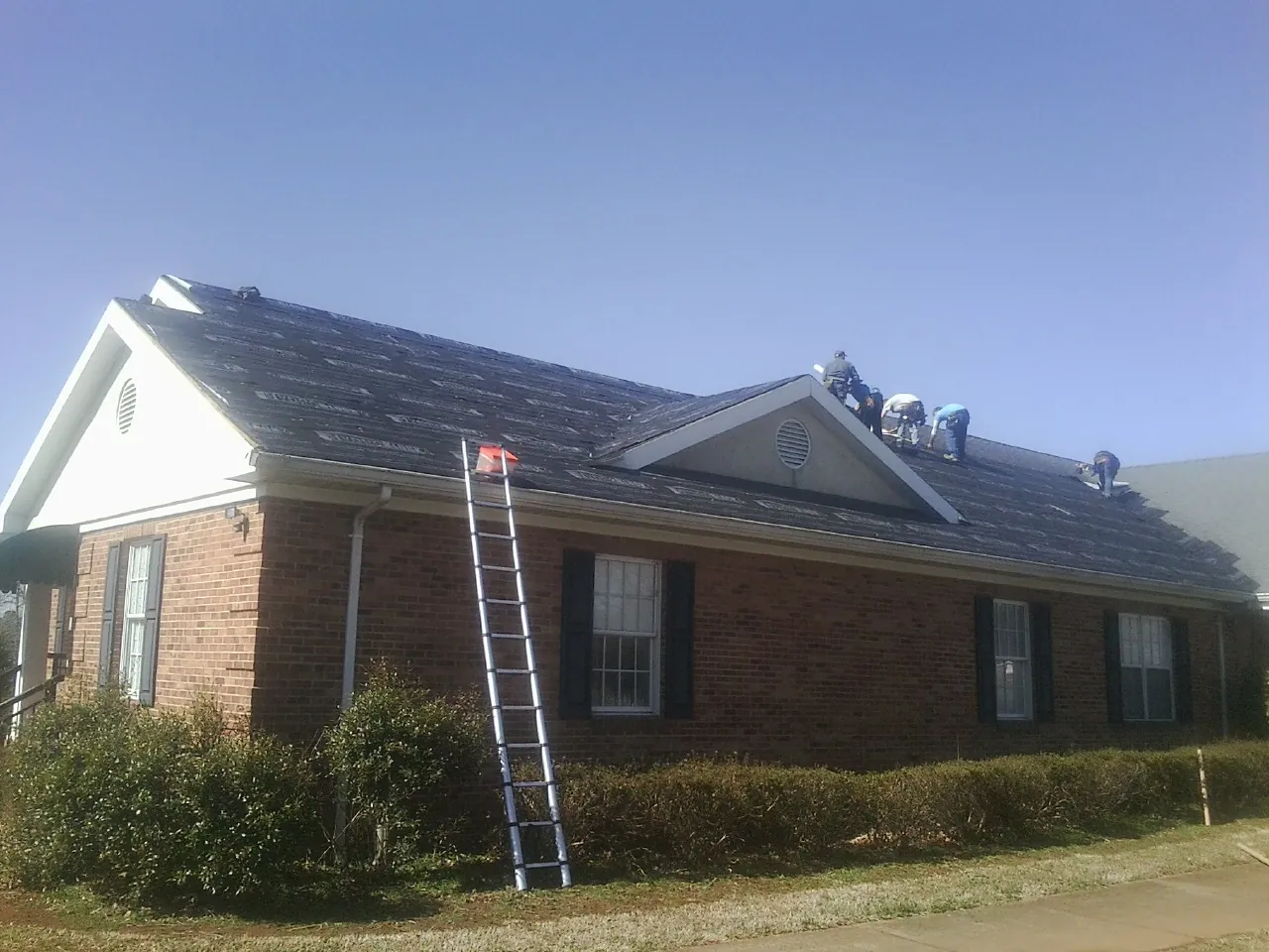 Crew tearing shingles off a brick ranch roof with a ladder set — Metal Roof Repair work by our crew in Chestnut Mound