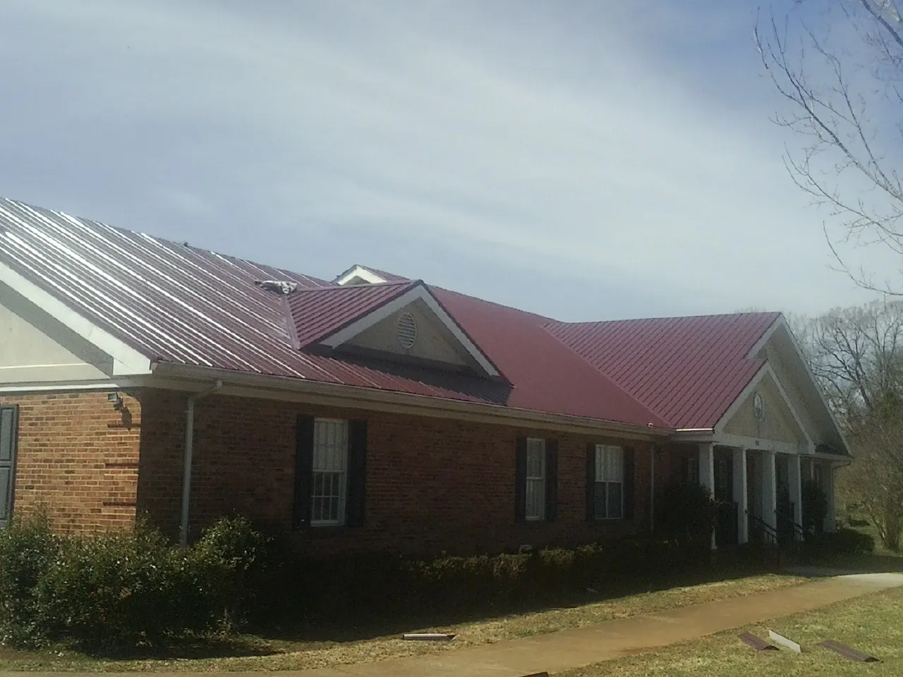 Red metal roof with gabled entries on a long brick building, from a Hail Damage Roof Repair job in Chestnut Mound