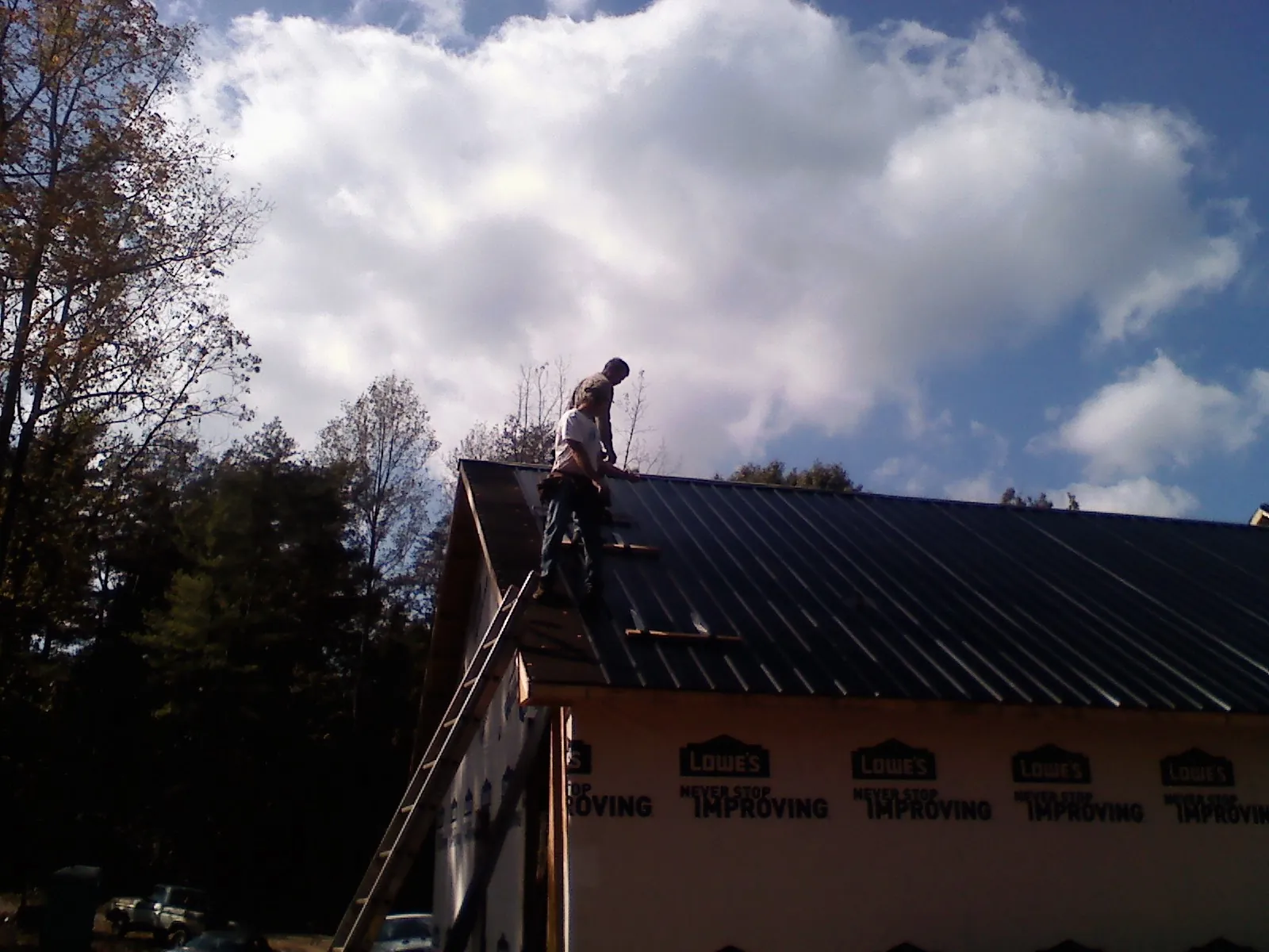Roofer fastening dark metal panels high against a cloudy sky, from a Roof Inspection job in Chestnut Mound