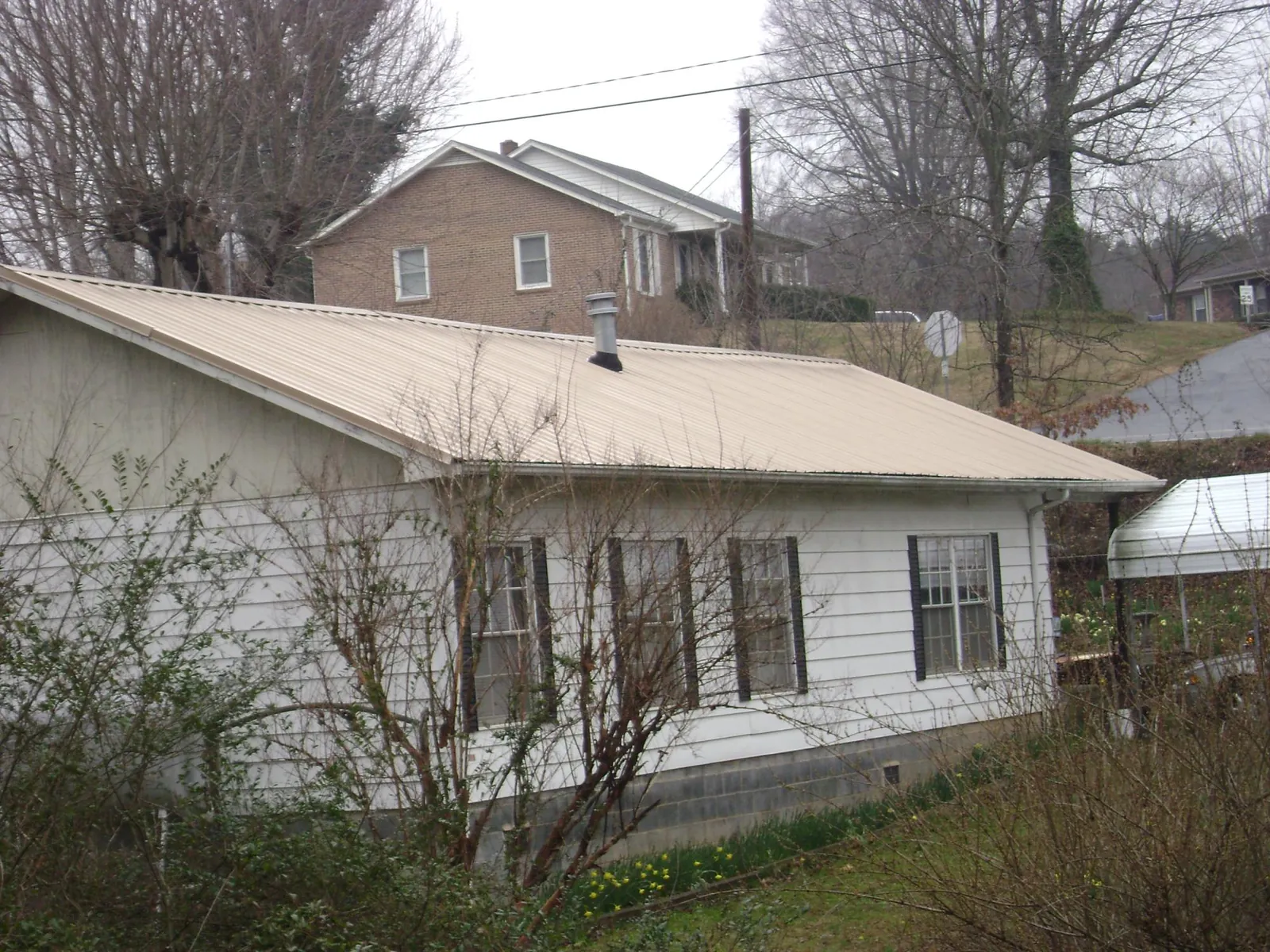 Tan metal roof on a white sided house set into a hillside — Commercial Roofing by Roofing Brothers in Chestnut Mound