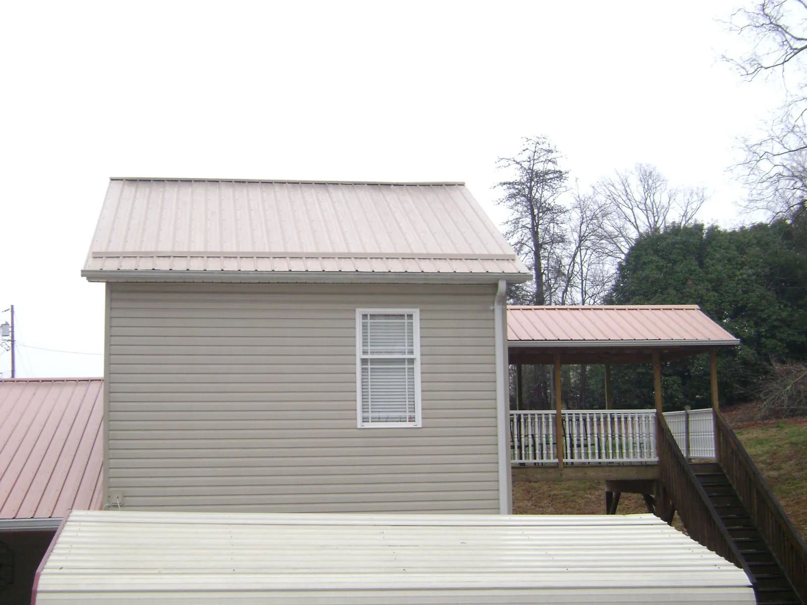 Tan metal roofs on a two story addition and attached porch, from a Roof Replacement job in Chestnut Mound